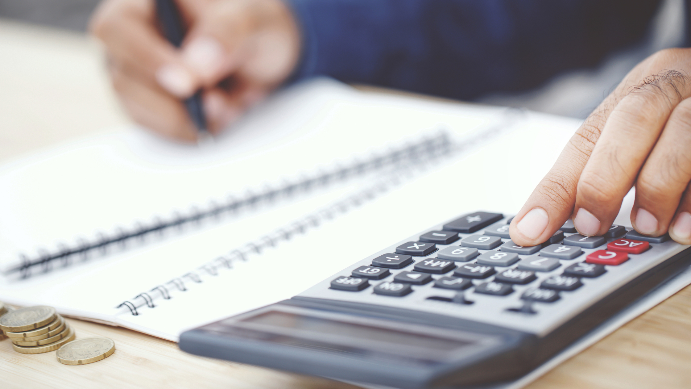 an accounts administrator using a calculatir to make calculations with coins in the foreground to represent savings