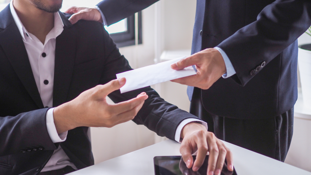A man in a suit handing an envelope as part of Corporate rewards and recognition programs to another man in a professional setting