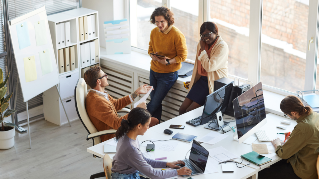 A group of employees in an office being productive and discussing projects using laptops