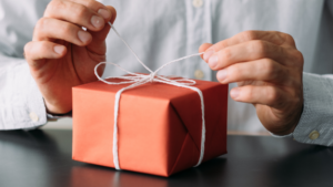 Close-up of hands tying a white ribbon on a red gift box, symbolizing the personal touch of corporate gift cards for employees.