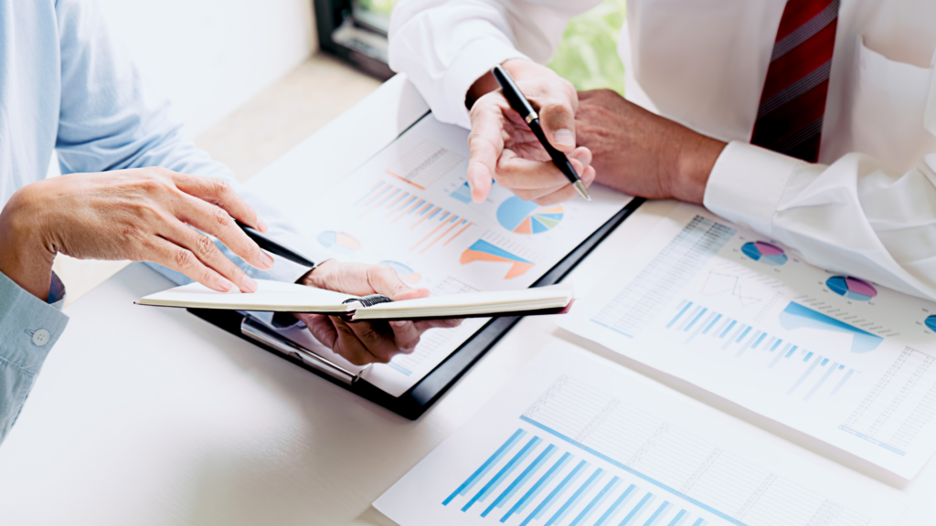 An image of two people examining charts on a computer monitor. One is pointing towards the chart that is indicating an upwards trend.