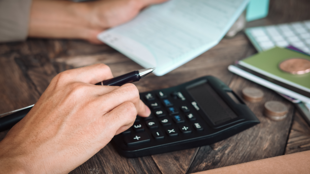 A person using a calculator on a desk beside papers and a cup.