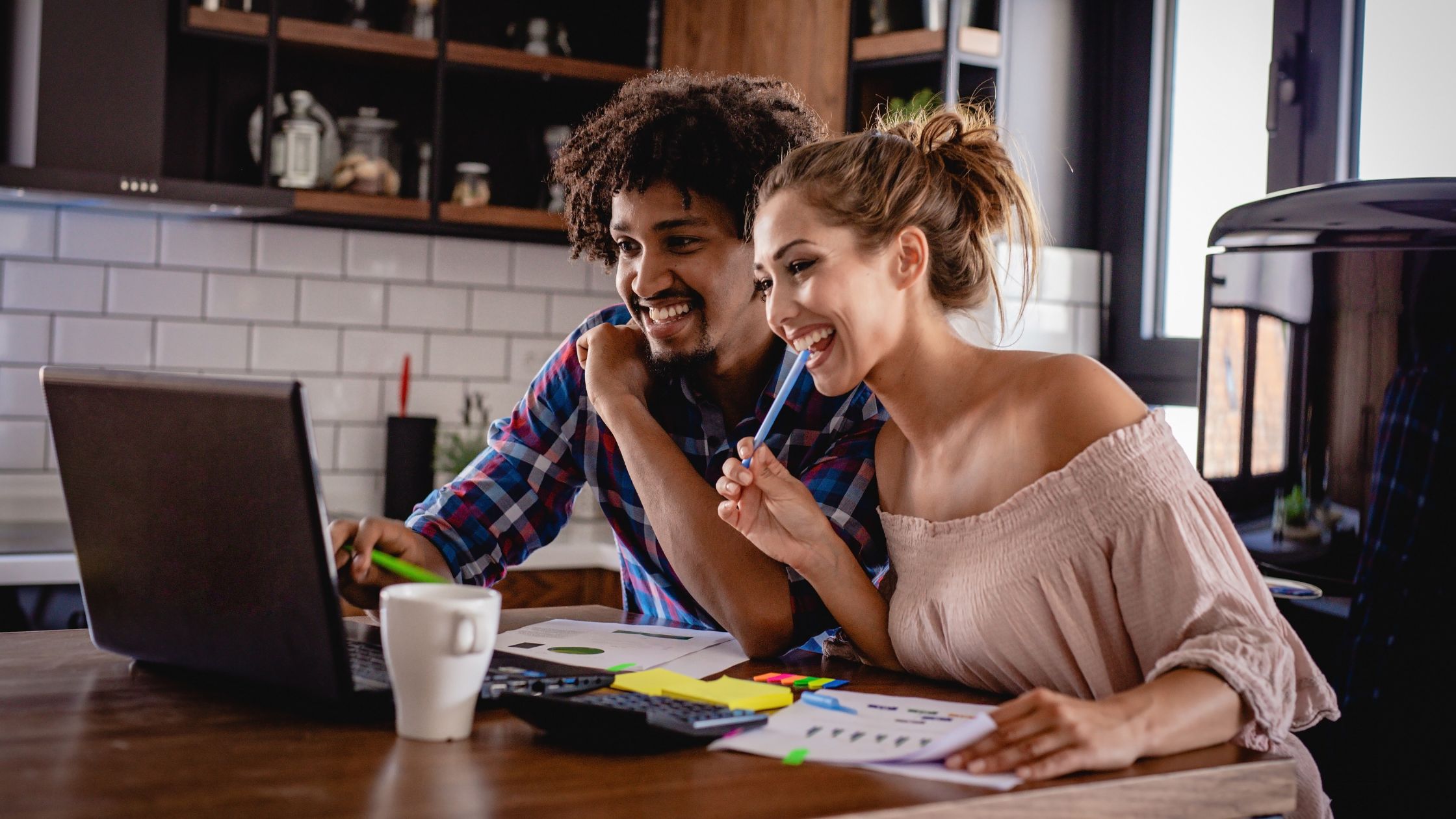 The image shows a man and a woman managing their expenses. They have a laptop in front of them with chart sheets and sticky notes on the table.